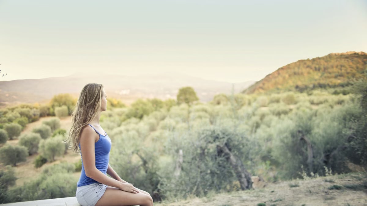 A woman in casual attire sits peacefully, enjoying a scenic outdoor view of nature.